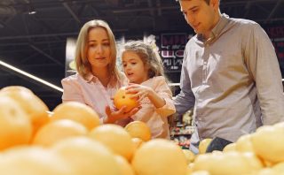 Parents and child selecting fresh oranges together at the supermarket. Captures family bonding and healthy shopping.