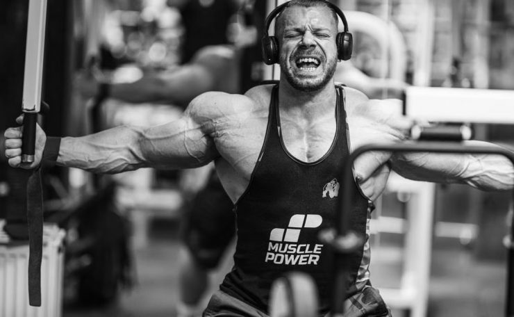 Muscular man intensely working out with gym equipment, showcasing strength and focus.